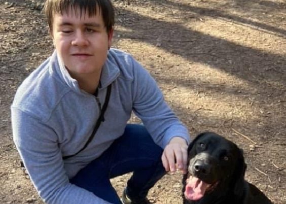 Kelsey kneeling down next to his black dog